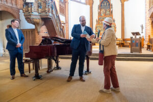 Uschi Becker überreicht Tom Kessler den Band Töster Blicke, Kai Schöneweiß schaut zu.